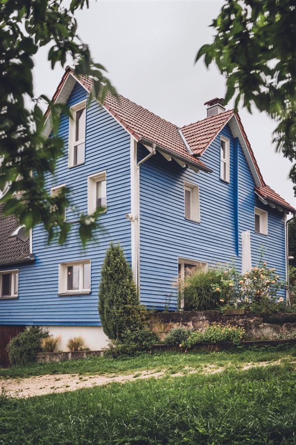Das Bronnenhaus heute mit seiner blauen Holzfassade und Rosen im Garten