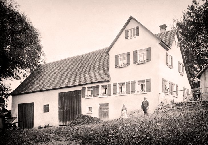 Historische Schwarzweißaufnahme des Bronnenhauses mit zwei Personen davor
